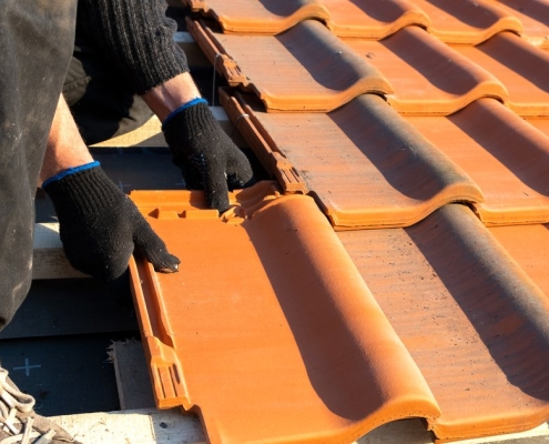 Couvreur installant des tuiles en terre cuite sur les liteaux lors d'une réfection de toiture en PACA